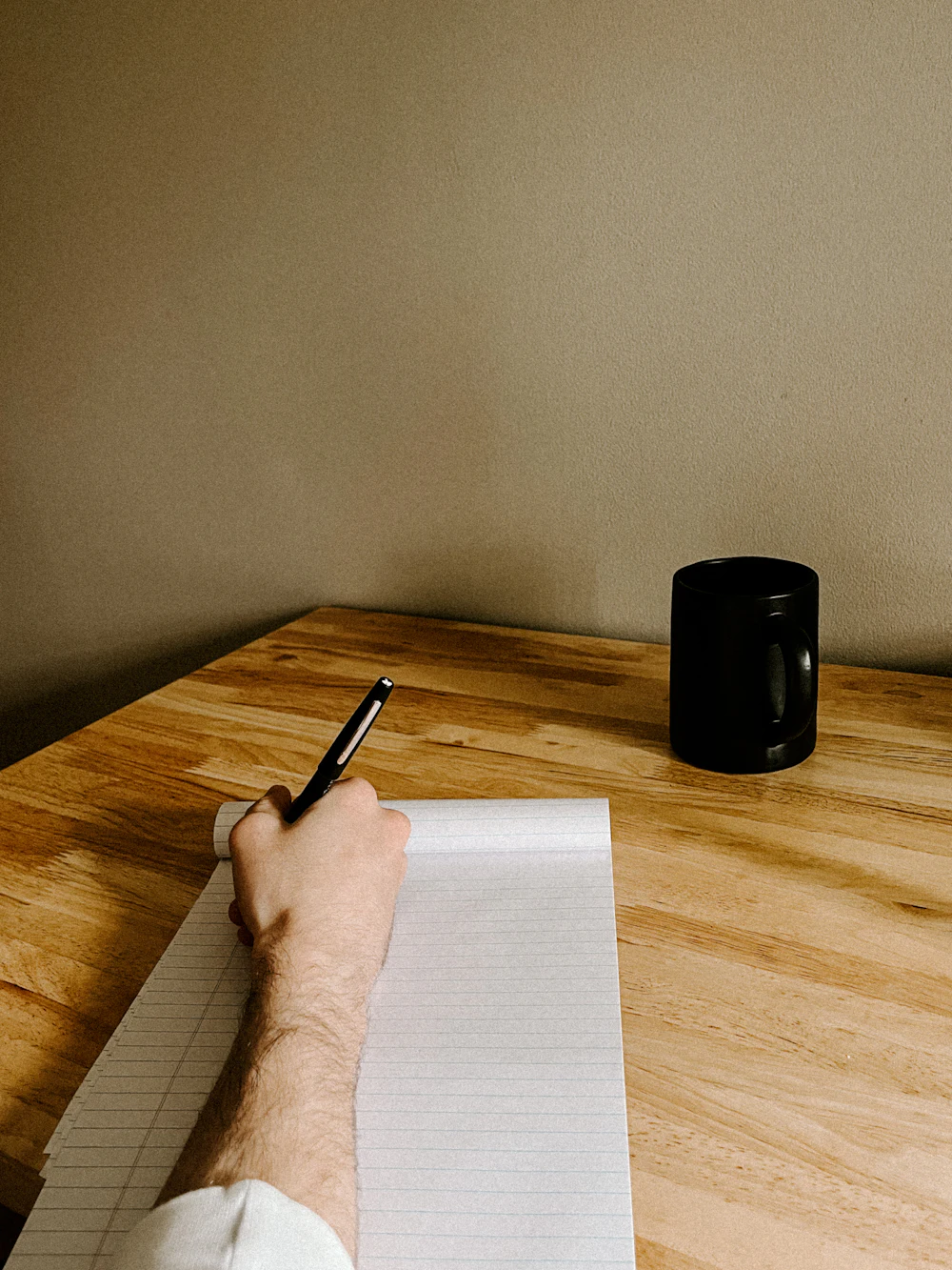 A hand writing notes on paper at a wooden desk
